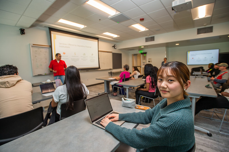 Student sitting at a table in a classroom with a laptop